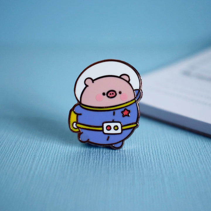 Space Pig enamel pin on blue table with notepad