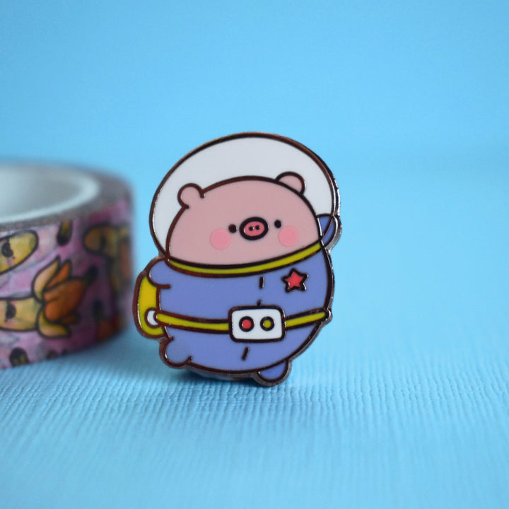 Space Pig enamel pin on blue desk with washi tape