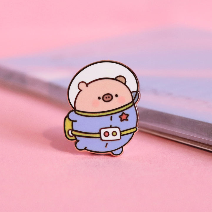 Space Pig enamel pin on pink table with notepad