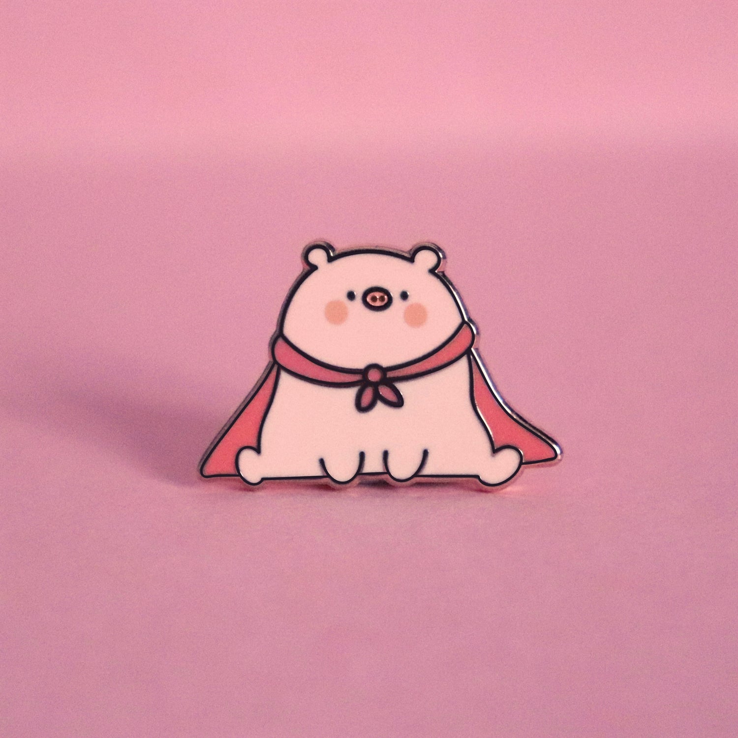 Super pig wearing red cape enamel pin on pink desk