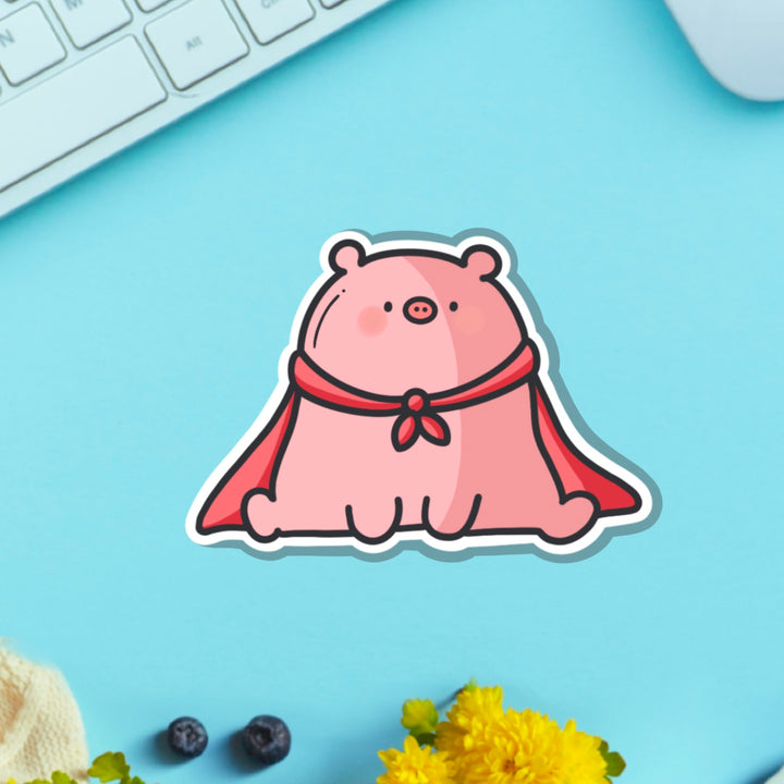 Super pig in red cape vinyl sticker on blue table with keyboard