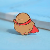 Super potato in red cape enamel pin on blue table with notepad