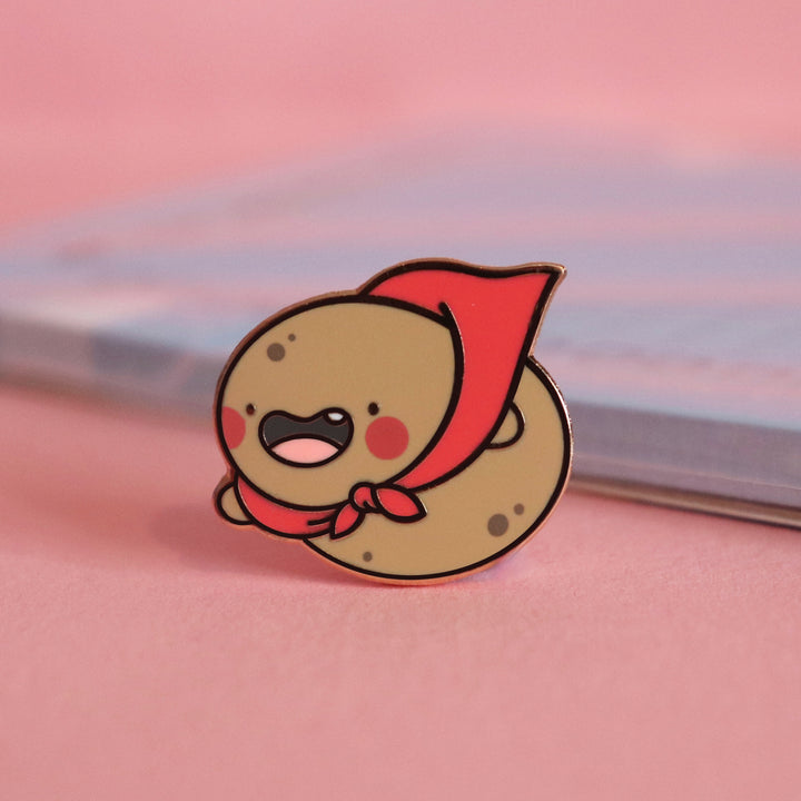 Super Potato enamel pin on pink desk with notepad
