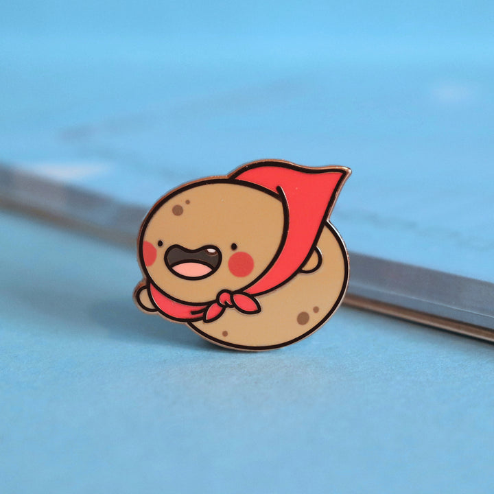 Super Potato enamel pin on blue table with notepad