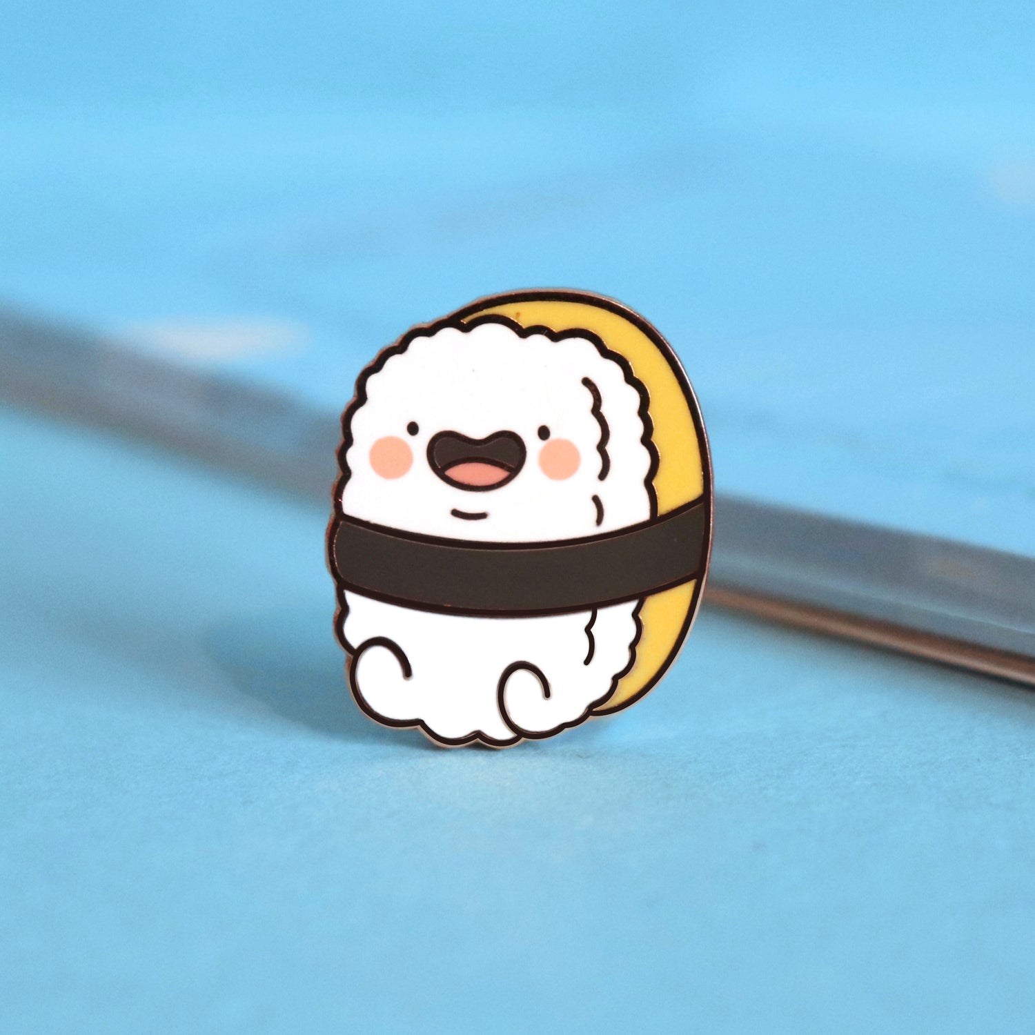 Sushi enamel pin on blue table with notebook
