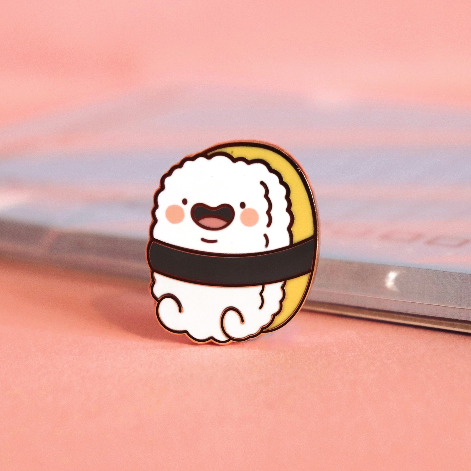 Sushi enamel pin on pink table with notebook