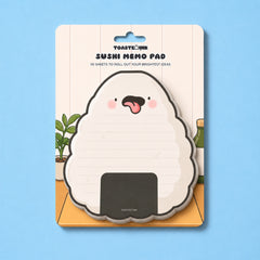 A packaged Toastink Sushi Memo Pad featuring a cute onigiri (rice ball) design with a pink tongue and cheeks, set against a light blue background.