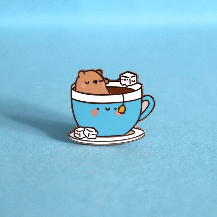 Bear sat in a cup of tea enamel pin on blue table