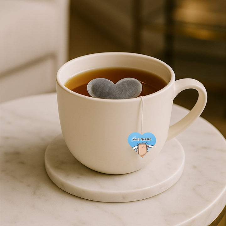 White mug with a heart-shaped tea bag on a marble coaster