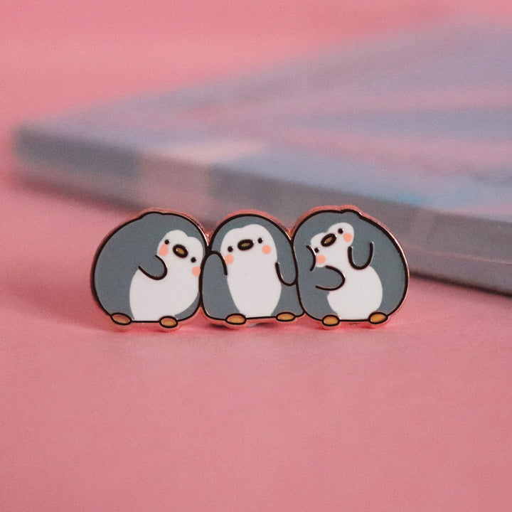 Three penguins enamel pin on pink desk with notepad