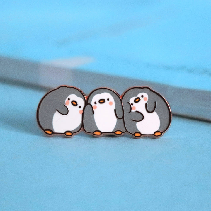 Three penguins enamel pin on blue table with notepad