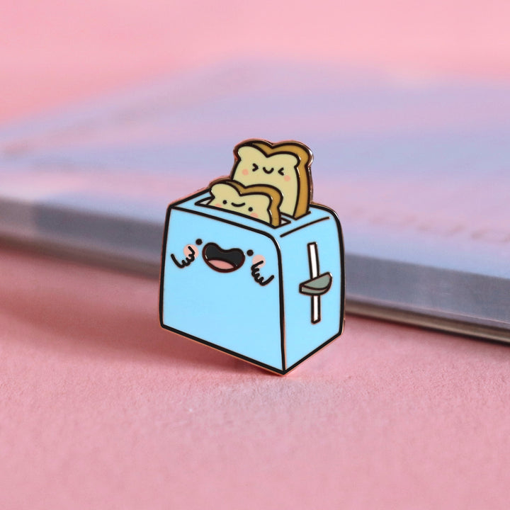 Toaster enamel pin on pink table with notepad