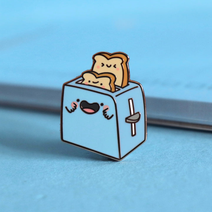 Toaster enamel pin on blue table with notepad