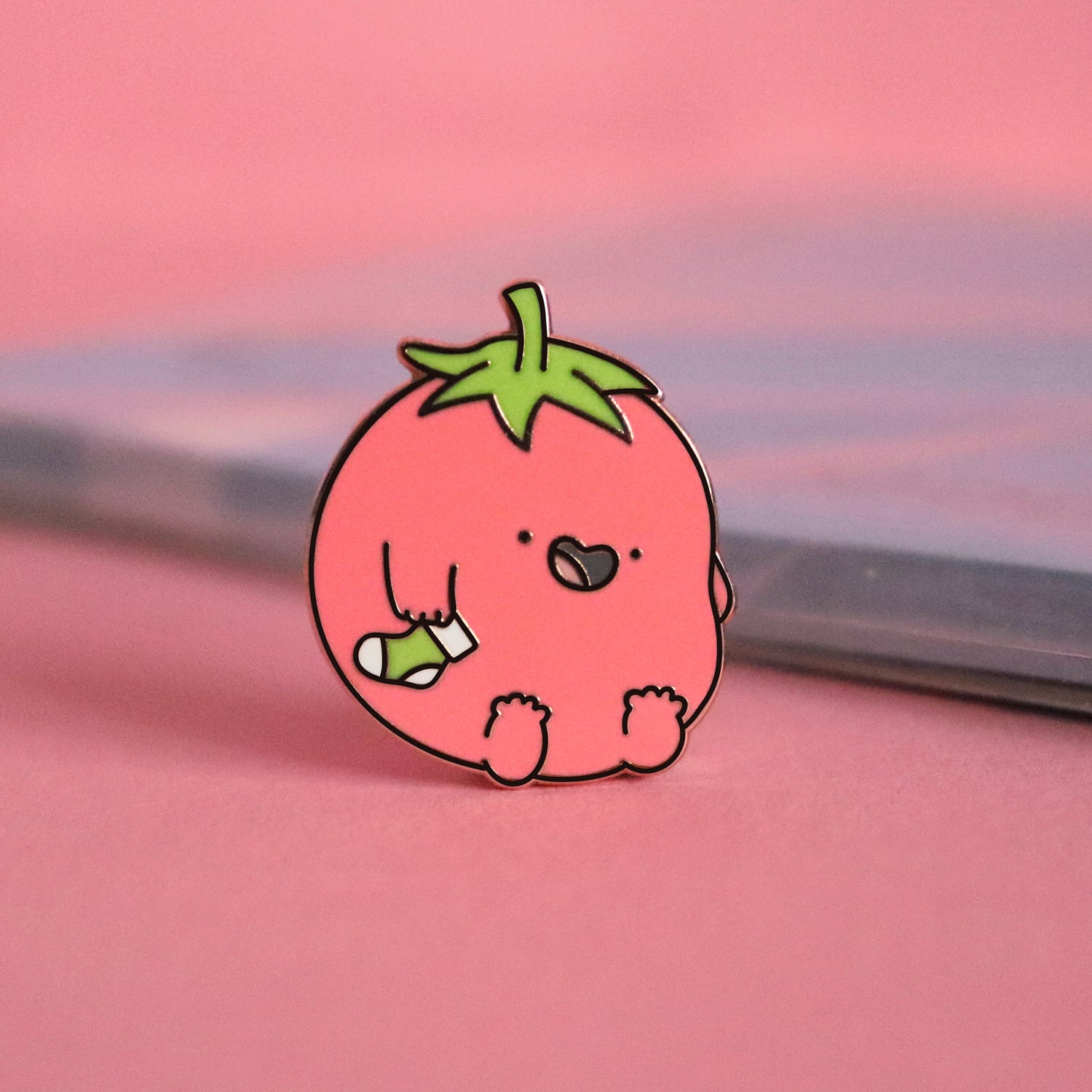 Tomato enamel pin on pink table with notepad