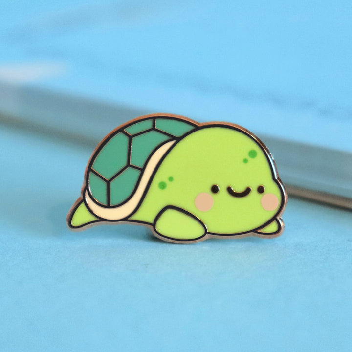 Turtle enamel pin on blue table with notepad