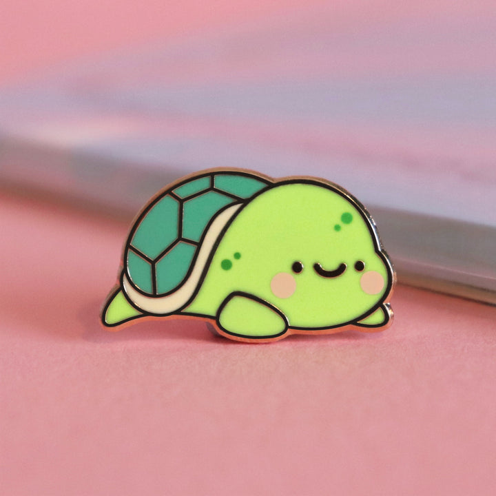 Turtle enamel pin on pink table with notepad