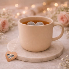 Beige mug with heart shaped tea on a marble coaster, surrounded by flowers and fairy lights