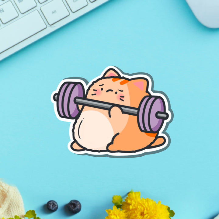 Cat lifting weights vinyl sticker on blue table with keyboard