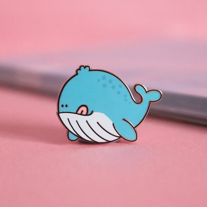 Whale enamel pin on pink table with notepad