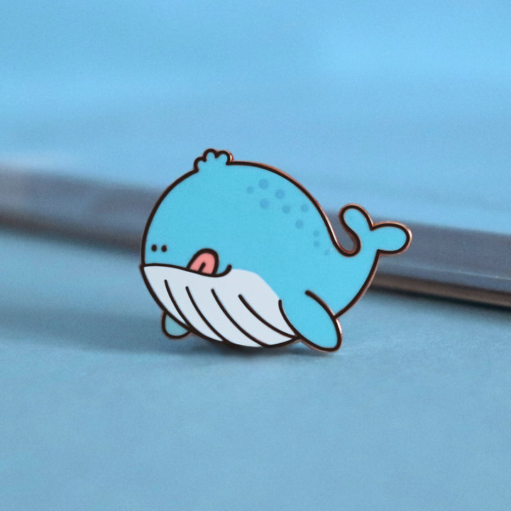 Whale enamel pin on blue table with notepad