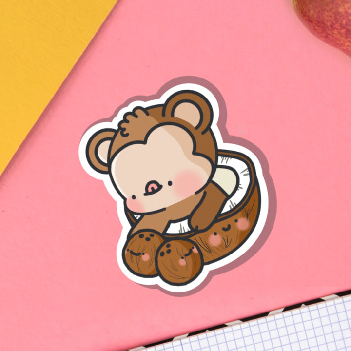 Monkey sat in coconut vinyl sticker on pink table and notebook