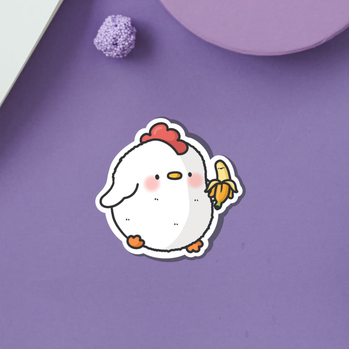 Chicken holding banana vinyl sticker on purple table
