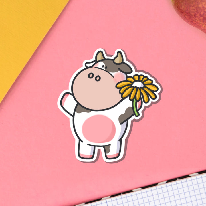 Cow holding flower vinyl sticker on pink table and notebook