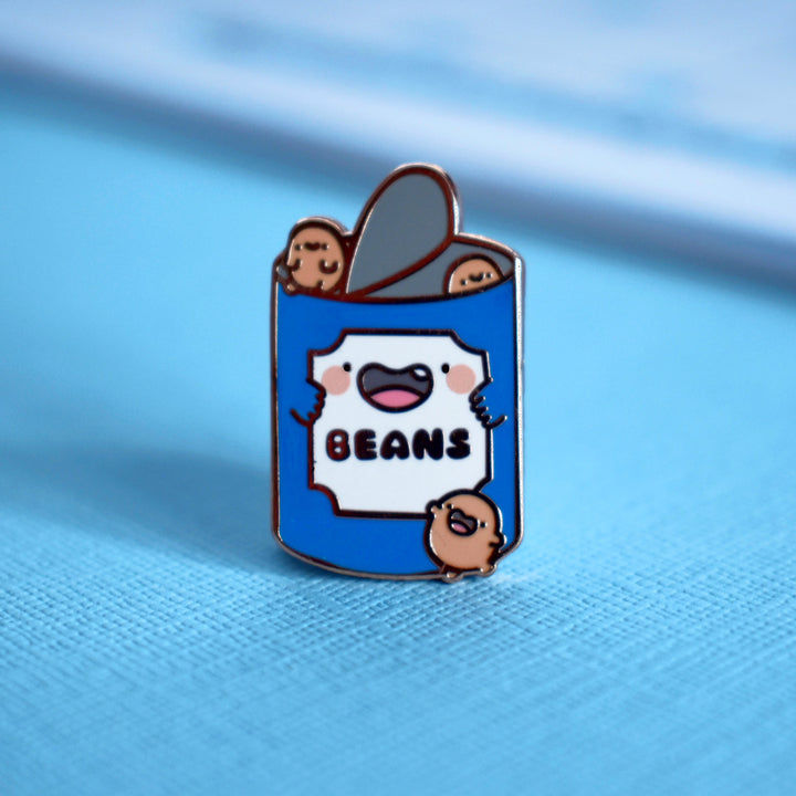 Cute Beans Pin propped up on a blue background