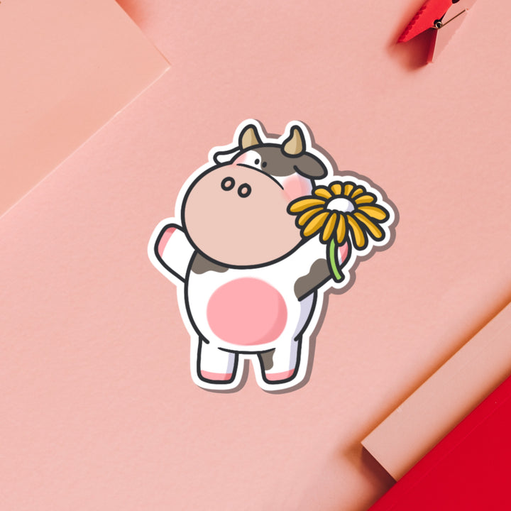 Cow holding flower vinyl sticker on pink table and notebook