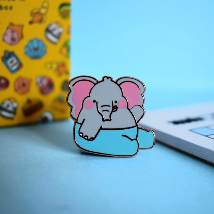 Elephant enamel pin with notebook on blue table