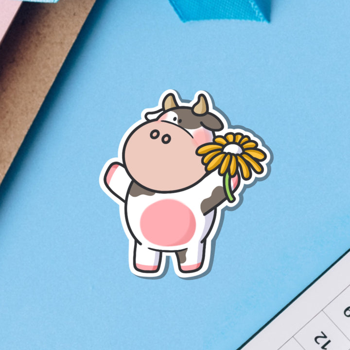 Cow holding flower vinyl sticker on blue background