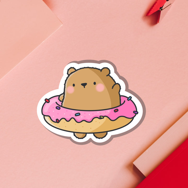 Bear wearing a donut vinyl sticker on pink table