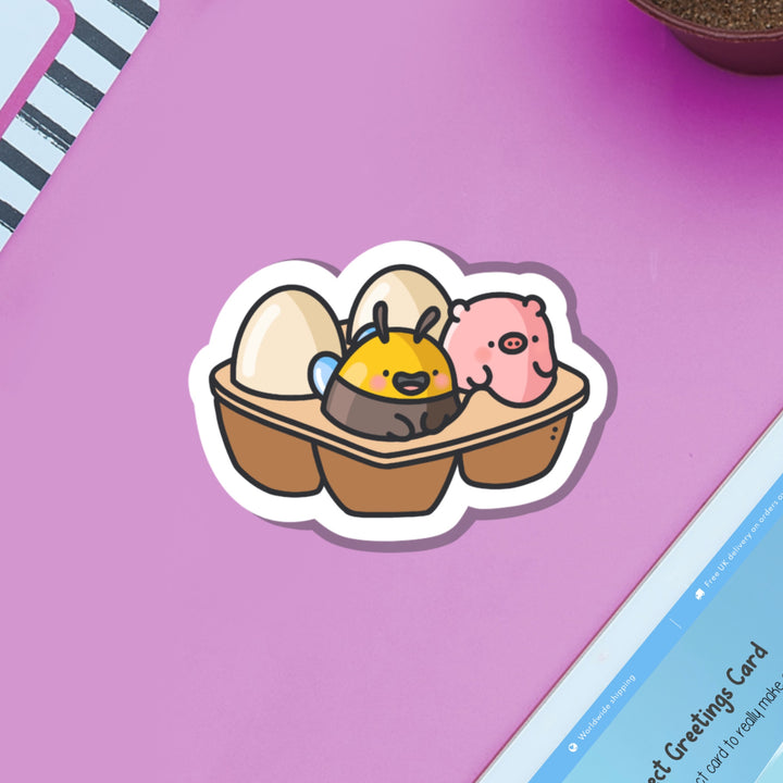 Egg carton with pig and bee vinyl sticker on purple table with ipad