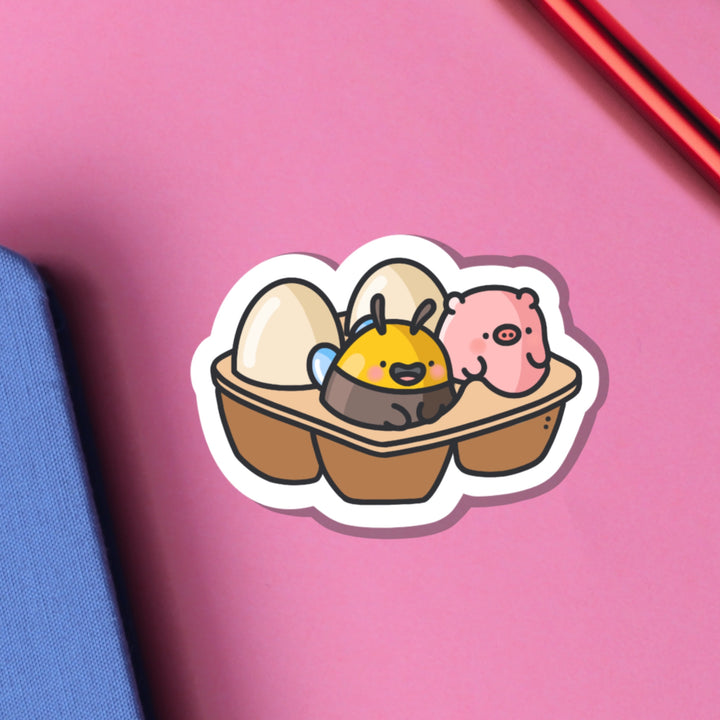 Egg carton with pig and bee vinyl sticker on pink table with ntoebook