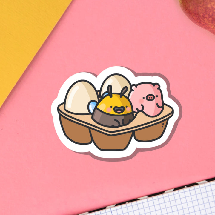 Egg carton with pig and bee vinyl sticker on pink table with notebook