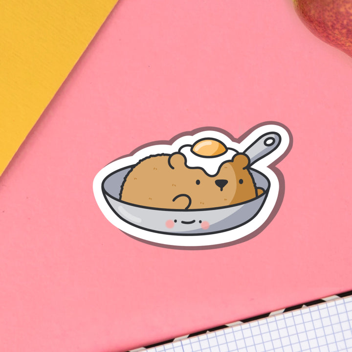 Bear in a frying pan vinyl sticker on pink table and notebook