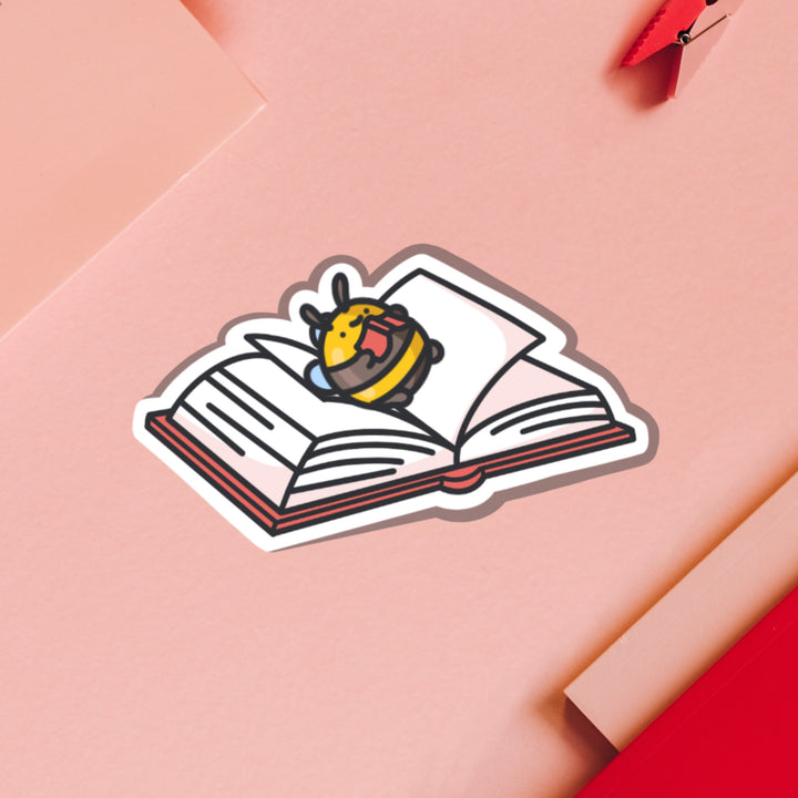 Bee lying on a book vinyl sticker on pink table