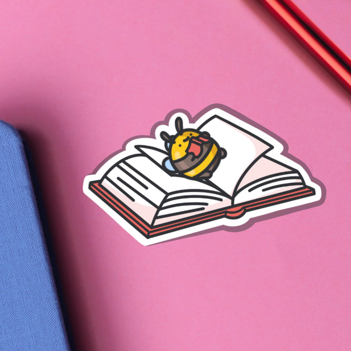 Bee lying on a book vinyl sticker on pink table