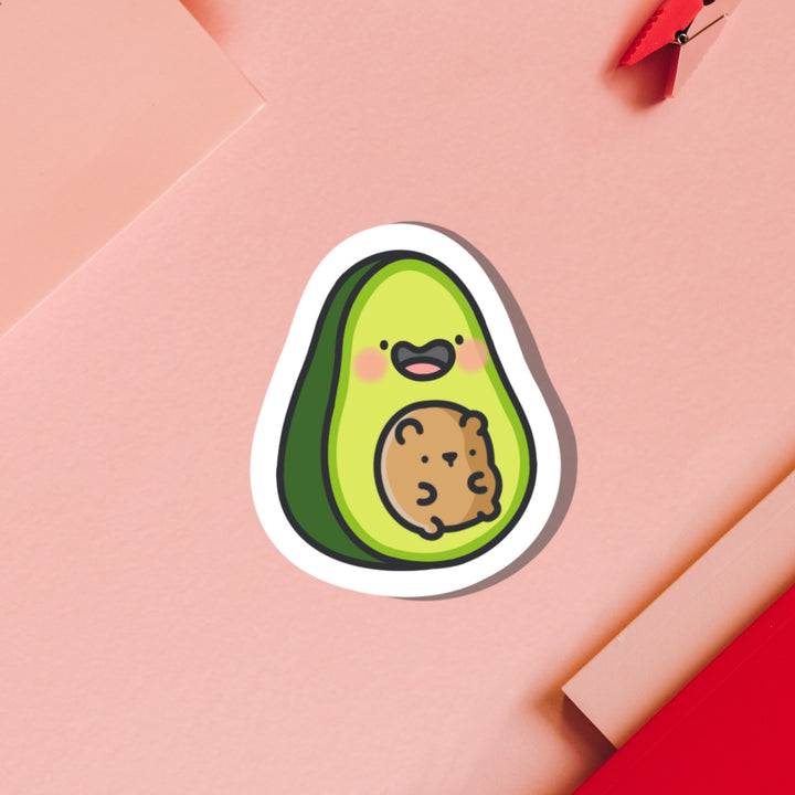 Avocado with bear vinyl sticker on pink table with notebook