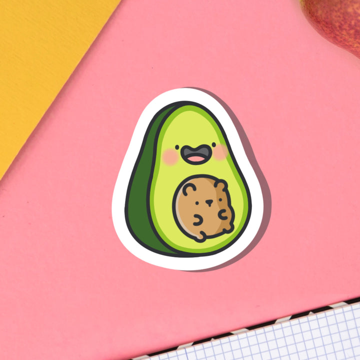 Avocado with bear vinyl sticker on pink table with notebooks
