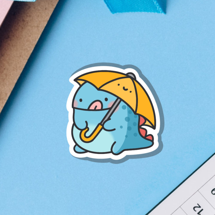 Dinosaur holding umbrella vinyl sticker on blue table 