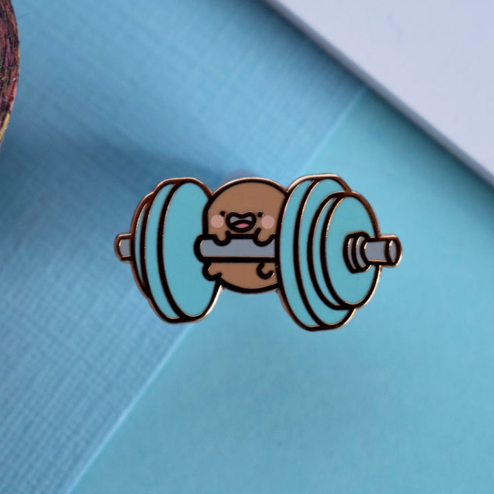 Potato holding weights enamel pin on blue table