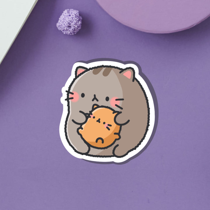 Cat holding baby kitty vinyl sticker on purple table