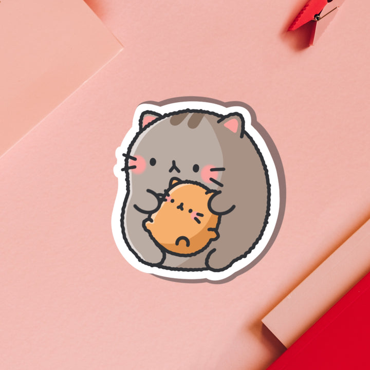 Cat holding baby kitty vinyl sticker on pink table