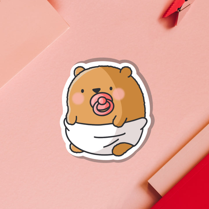 Bear dressed as baby vinyl sticker on pink table with notebook