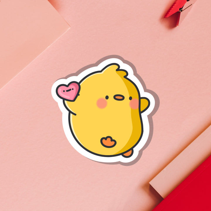 Chick holding heart vinyl sticker on pink table