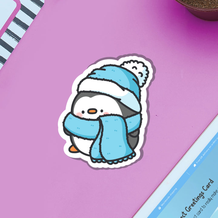 Penguin in scarf and wooly hat vinyl sticker on purple table and ipad