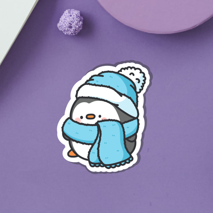 Penguin in scarf and wooly hat vinyl sticker on purple table