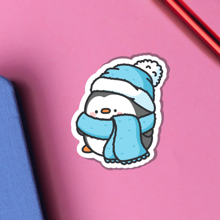 Penguin in scarf and wooly hat vinyl sticker on pink table