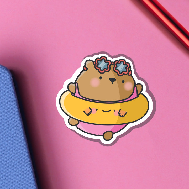 Bear dressed in beach outfit vinyl sticker on pink table on notebook